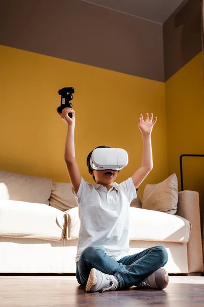 KIEV, UKRAINE - 22 AVRIL 2020 : joyeux garçon jouant à un jeu vidéo avec manette de jeu et casque de réalité virtuelle sur l'auto-isolement — Photo de stock