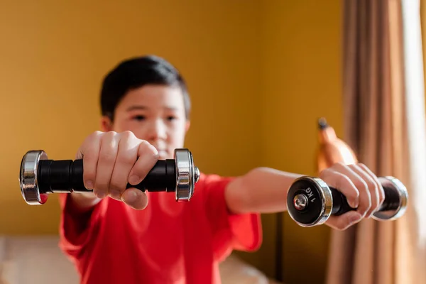 Sportive asian boy exercising with dumbbells at home during self isolation, selective focus — Stock Photo