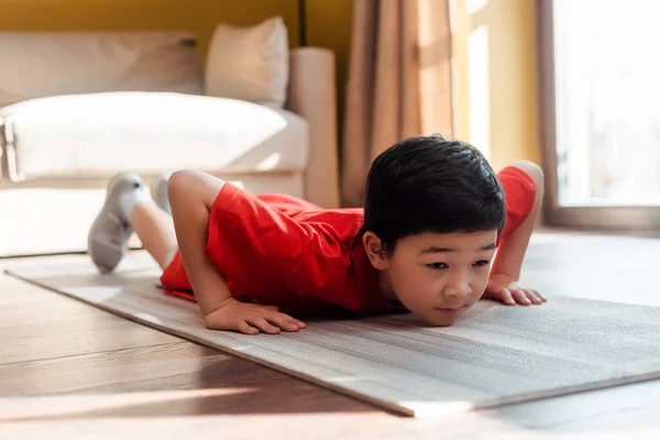 Sportive asian boy doing push ups on fitness mat at home during self isolation — Stock Photo