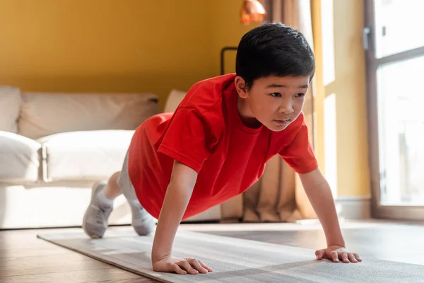 Sportive asian kid doing push ups on fitness mat at home during self isolation — Stock Photo