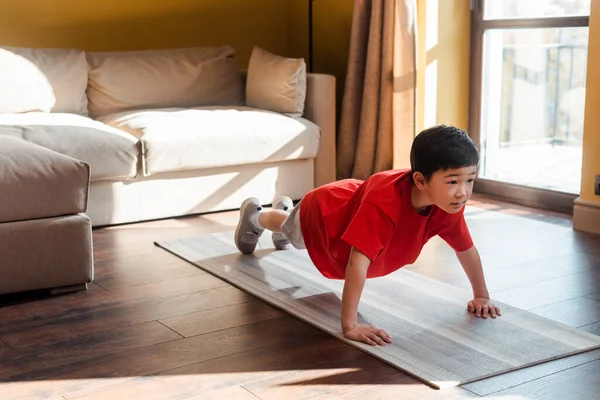 Adorable sportive asian boy doing plank on fitness mat at home during self isolation — Stock Photo