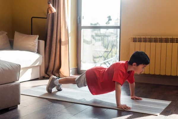 Атлетичный мальчик занимается дома на фитнес-коврике во время самоизоляции — стоковое фото