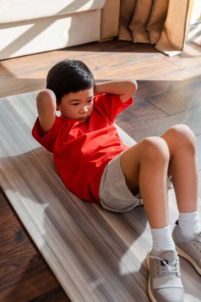 Sporty asian boy doing abs on fitness mat at home during self isolation — Stock Photo