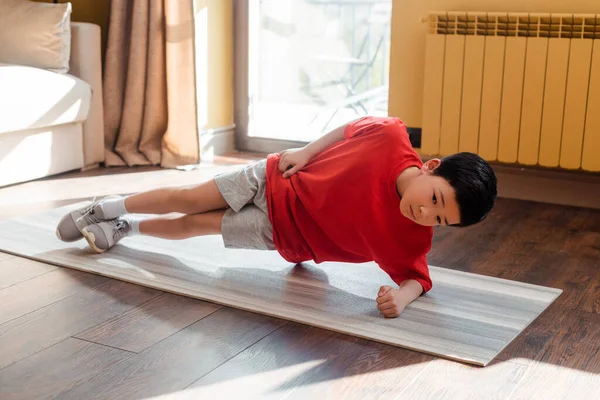 Sportivo asiatico capretto fare lato tavola su fitness mat a casa durante auto isolamento — Foto stock