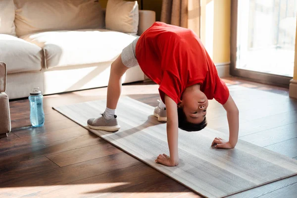 Un garçon asiatique dans un pont pose sur un tapis de conditionnement physique à la maison pendant la quarantaine — Photo de stock