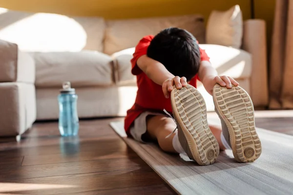 Мальчик растягивается на фитнес-коврике со спортивной бутылкой дома во время карантина — стоковое фото