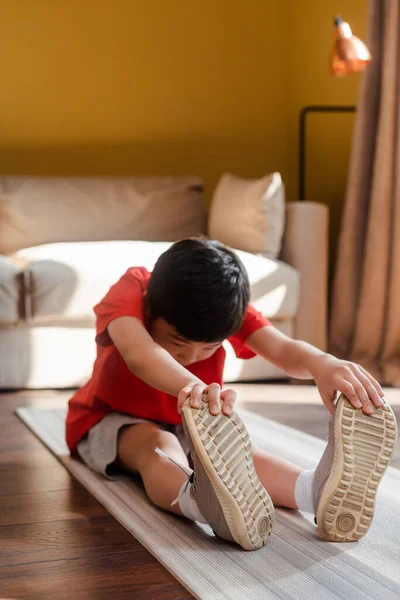 Спортивный ребенок, растягивающийся на фитнес-коврике дома во время самоизоляции — стоковое фото