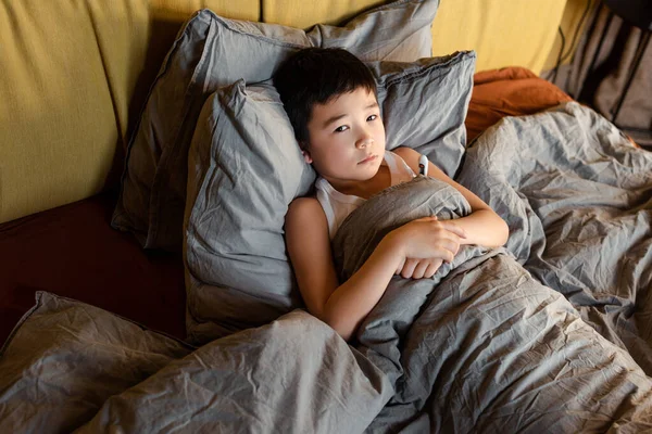 Chico asiático triste con termómetro acostado en la cama sobre aislamiento personal. - foto de stock