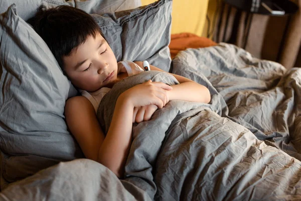 Втомлений хворий азіатський хлопчик з термометром спить у ліжку на самоізоляції — стокове фото