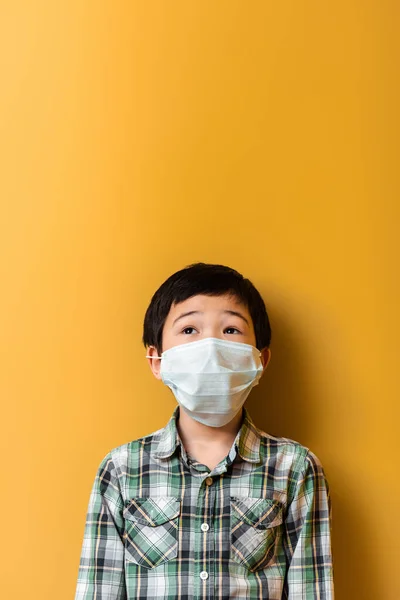 Surprised asian boy in medical mask on yellow during self isolation — Stock Photo