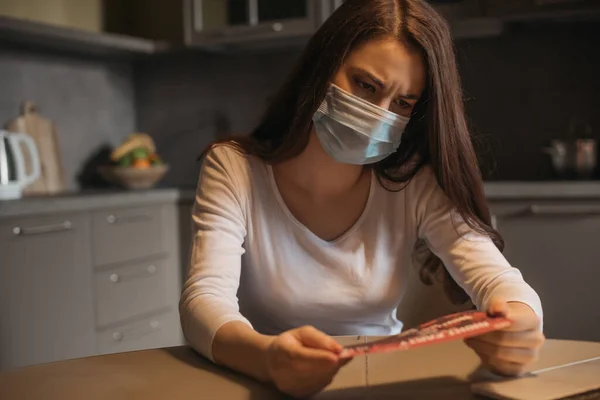 Вибірковий фокус сумної жінки в медичній масці, що тримає квитки вдома — стокове фото