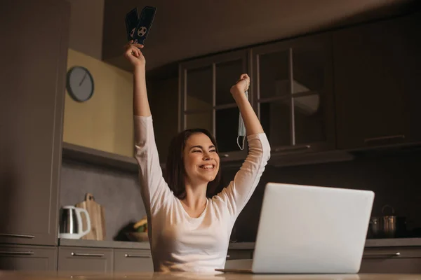 Freelancer feliz com as mãos acima da cabeça segurando bilhetes de jogo esporte perto do laptop, fim do conceito de quarentena — Fotografia de Stock