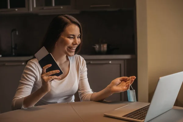 Happy freelancer holding passport with air ticket near laptop, end of quarantine concept — Stock Photo