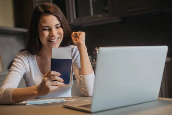 Enfoque selectivo de freelancer alegre con pasaporte con billete de avión cerca de la computadora portátil y máscara médica, fin del concepto de cuarentena - foto de stock