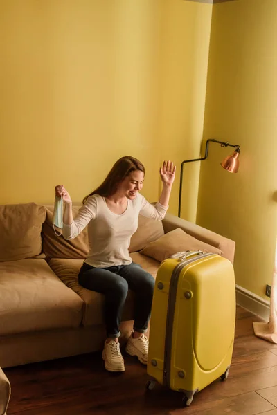 Happy woman with medical mask looking at luggage, end of quarantine concept — Stock Photo