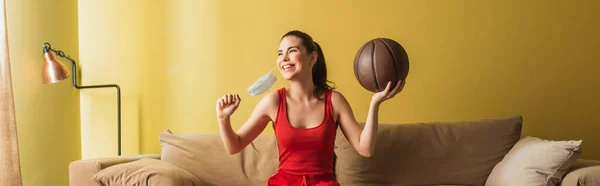 Tiro panorámico de deportista feliz tocando máscara médica y la celebración de baloncesto en la sala de estar, fin del concepto de cuarentena — Stock Photo