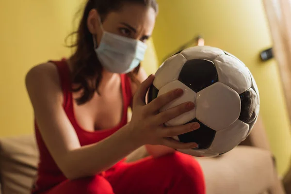 Selektiver Fokus der sportlichen Frau mit medizinischer Maske, die den Fußball zu Hause hält — Stockfoto