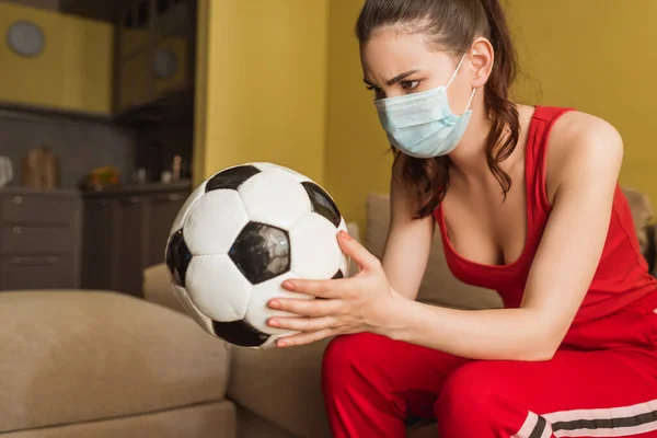 Sportive woman in medical mask looking at football at home — Stock Photo