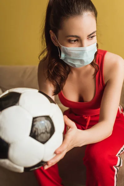 Selective focus of sportive girl in medical mask holding football at home — Stock Photo