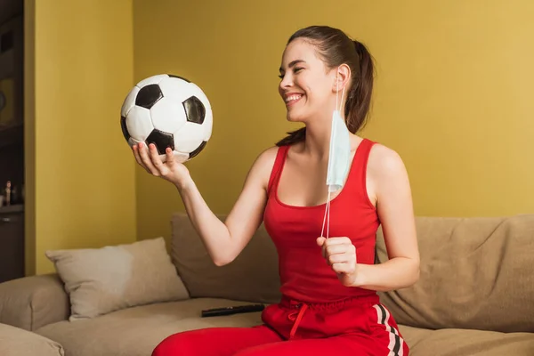 Felice sportiva toccando maschera medica e tenendo il calcio, fine del concetto di quarantena — Foto stock