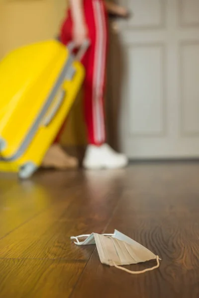 Selektiver Fokus der medizinischen Maske auf dem Boden in der Nähe der Frau mit Gepäck, Ende des Quarantäne-Konzepts — Stockfoto