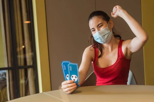 Donna allegra in maschera medica in possesso di biglietti partita sportiva — Foto stock