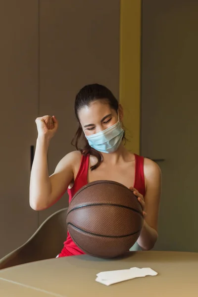 Sportive woman in medical mask and closed eyes cheering near basketball — Stock Photo