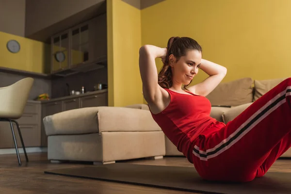 Mujer joven y feliz en ropa deportiva haciendo ejercicio en la alfombra de fitness - foto de stock