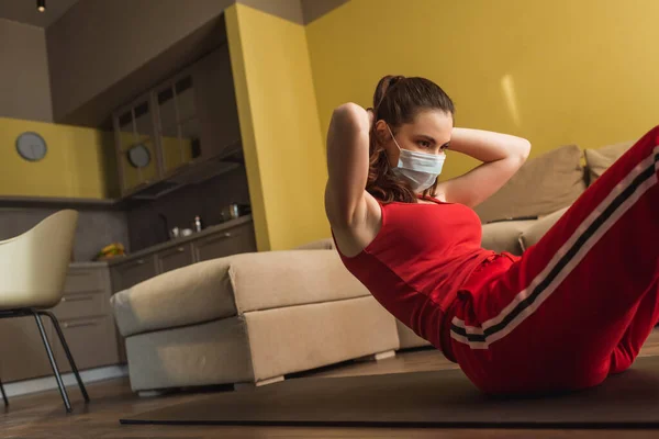 Jeune femme en masque médical et vêtements de sport travaillant sur tapis de fitness — Photo de stock