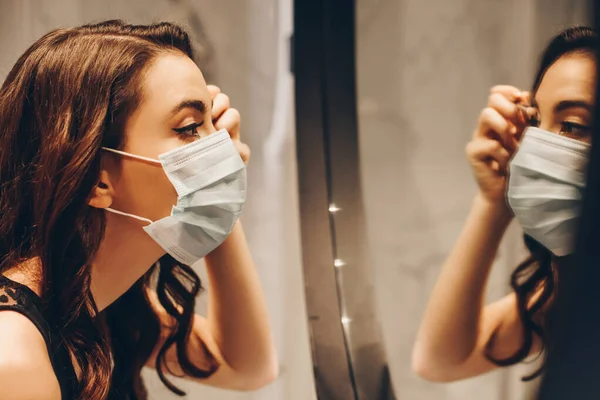 Selective focus of attractive woman in medical mask applying eye shadow in bathroom — Stock Photo