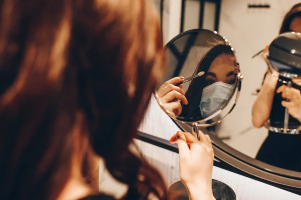 Selective focus of girl in medical mask applying eye shadow in bathroom — Stock Photo