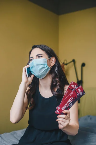 Menina em máscara médica segurando bilhetes de festa noturna e falando smartphone, fim do conceito de quarentena — Fotografia de Stock