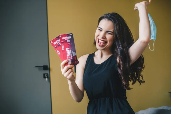 Menina animado em vestido preto segurando bilhetes de festa noite e máscara médica, fim do conceito de quarentena — Fotografia de Stock