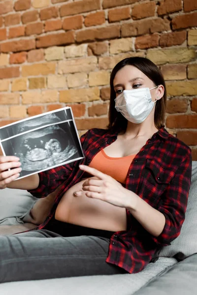 Foyer sélectif de la femme enceinte dans le masque médical pointant avec le doigt à l'échographie photos — Photo de stock