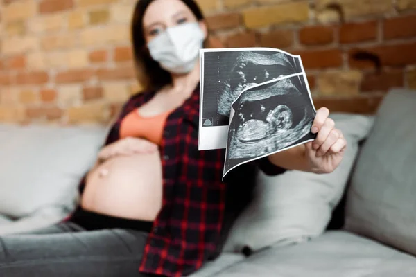 Selective focus of pregnant woman in medical mask holding ultrasound photos — Stock Photo