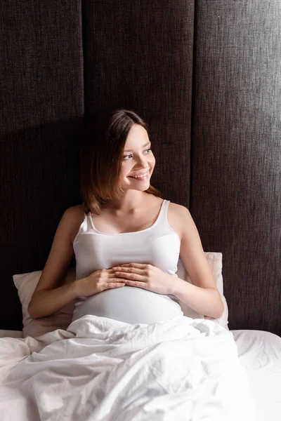 Happy and pregnant woman touching belly and looking away — Stock Photo
