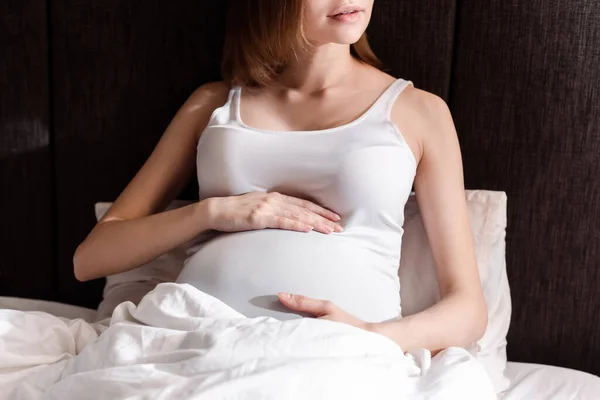 Ausgeschnittene Ansicht von schwangerer Frau, die Bauch im Bett berührt — Stockfoto