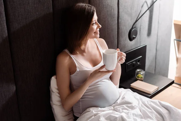 Happy pregnant woman holding cup of tea in bed — Stock Photo