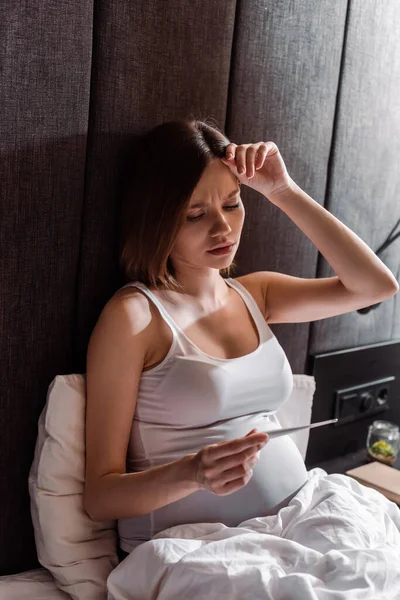 Donna incinta con termometro digitale in camera da letto — Foto stock