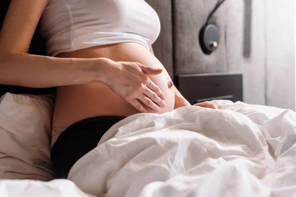 Vista recortada de la mujer embarazada tocando el vientre con gel en el dormitorio - foto de stock