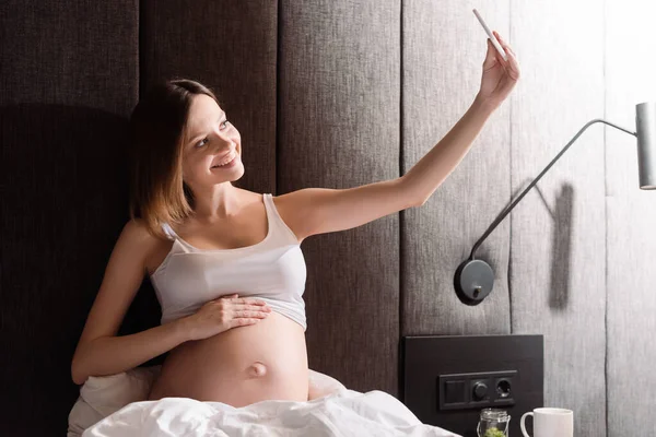 Glückliche und schwangere Frau macht Selfie im Schlafzimmer — Stockfoto