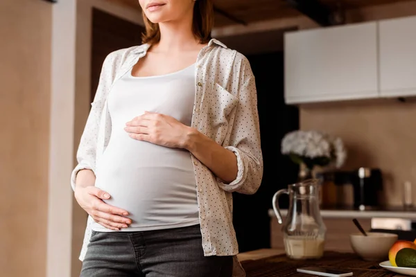 Abgeschnittene Ansicht einer schwangeren Frau, die ihren Bauch in der Nähe des Frühstücks am Tisch berührt — Stockfoto