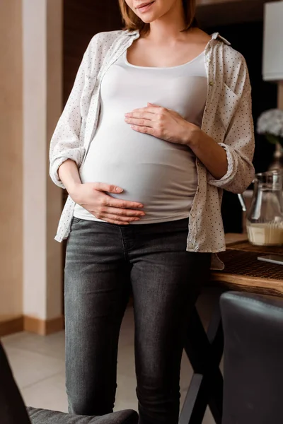 Abgeschnittene Ansicht einer schwangeren Frau, die ihren Bauch berührt, während sie zu Hause steht — Stockfoto