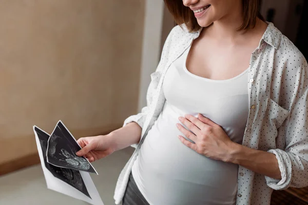Обрезанный вид счастливой и беременной женщины с ультразвуковыми фотографиями — стоковое фото