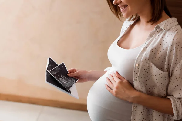 Обрізаний вид щасливої і вагітної жінки, що тримає ультразвукові фотографії — стокове фото