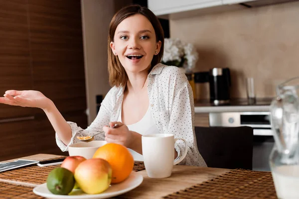 Enfoque selectivo de la mujer excitada sosteniendo cuchara con hojuelas de maíz cerca de frutas - foto de stock