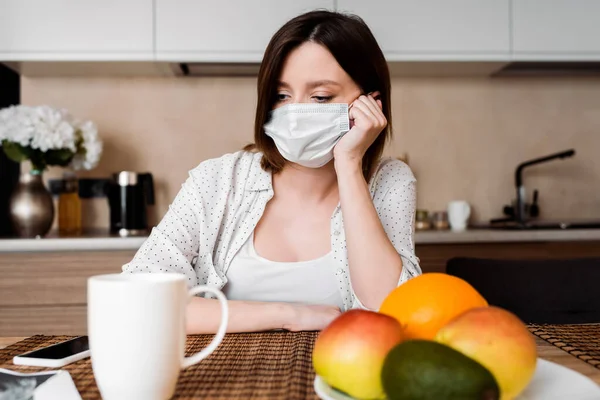 Messa a fuoco selettiva della donna incinta in maschera medica vicino smartphone con schermo bianco e frutta — Foto stock