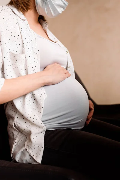Vista recortada de la mujer embarazada en máscara médica tocando el vientre - foto de stock