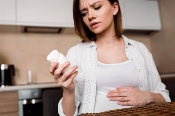 Foco seletivo da mulher grávida olhando para garrafa com vitaminas — Fotografia de Stock