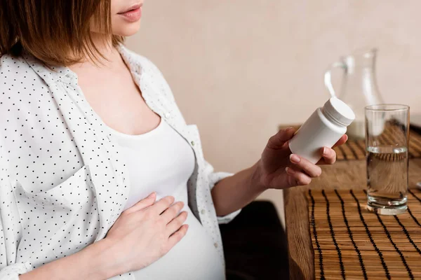 Обрізаний вид вагітної жінки, що тримає пляшку з вітамінами — стокове фото